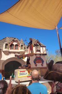 A person juggles in front of a crowd, standing on a precarious perch.