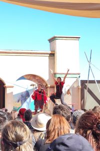 Two people in red and black perform in front of a large crowd.