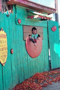 A man sticks his head through a hole in a teal wall.