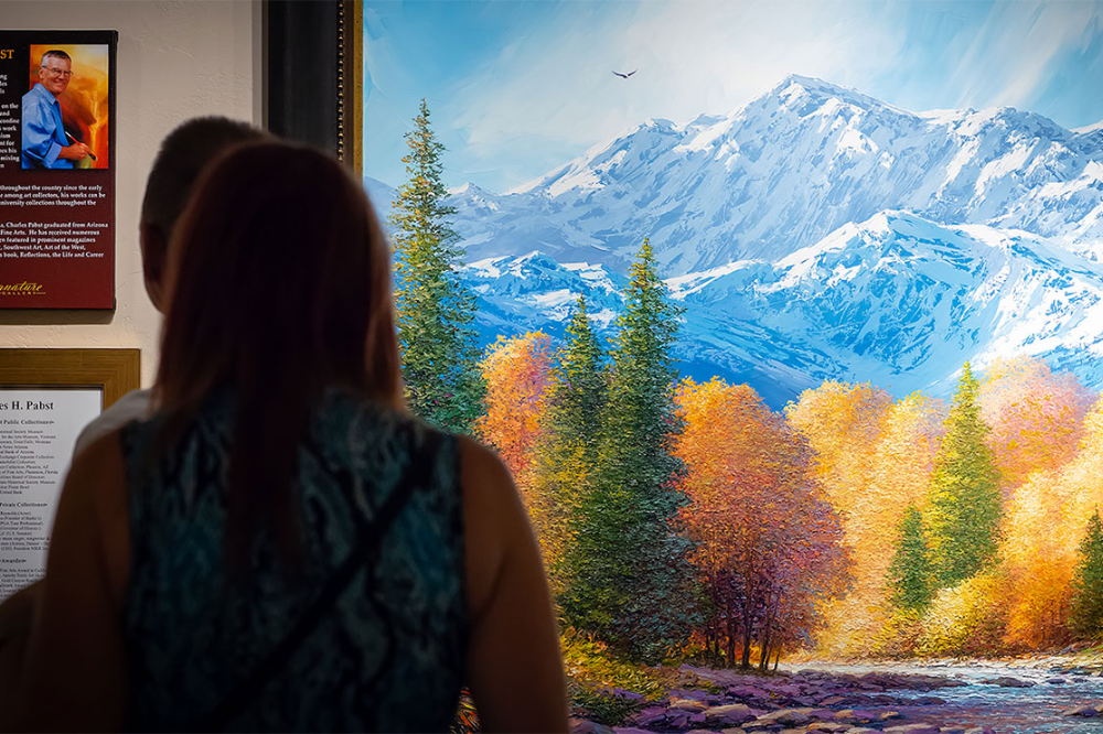 Woman looks at painting of mountains and fall trees. 